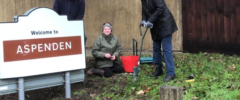 People planting bulbs next to village sign
